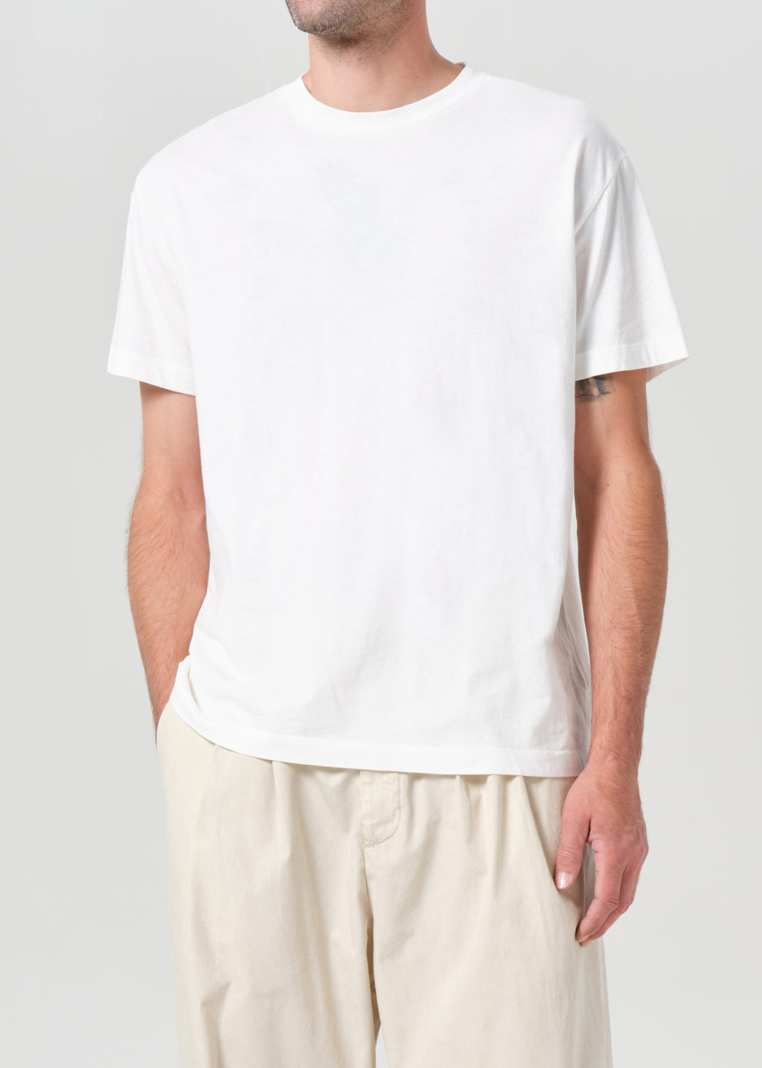 Person wearing a plain white t-shirt and light-colored pants on a neutral background