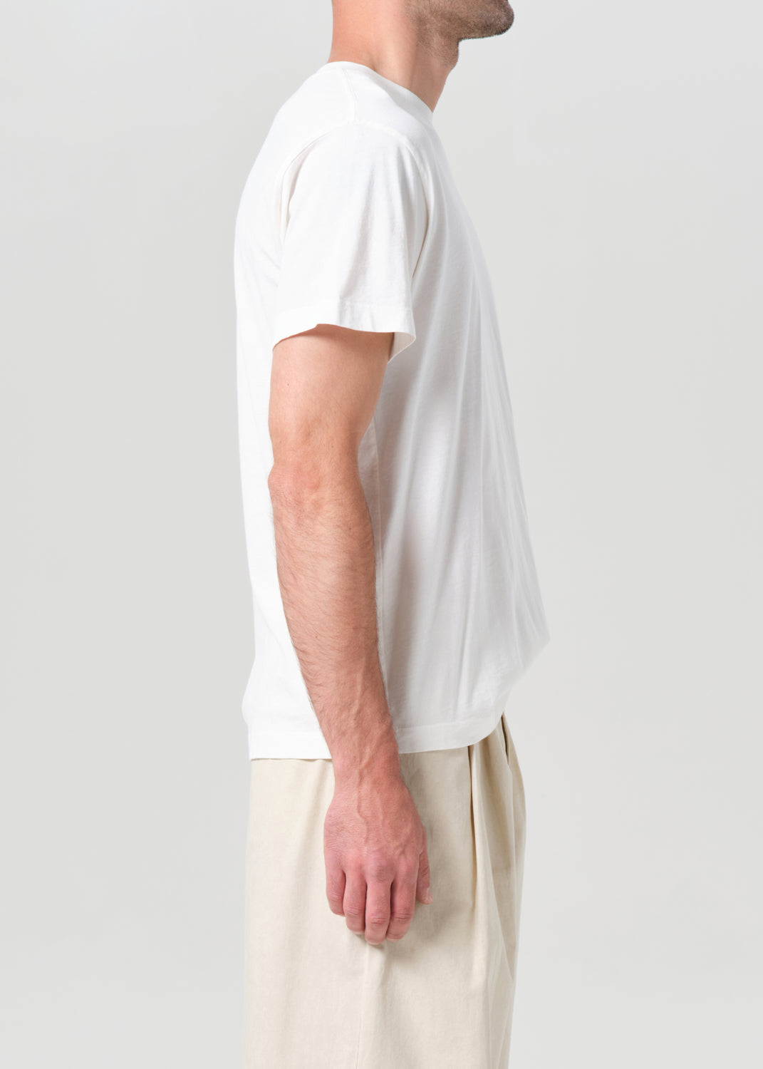 Person wearing a plain white t-shirt and light-colored pants on a light gray background