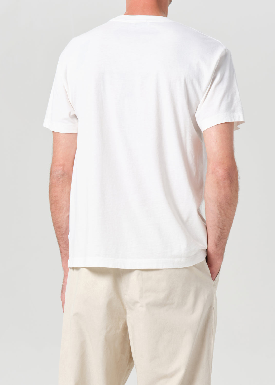 Person wearing a plain white t-shirt and light-colored pants on a neutral background