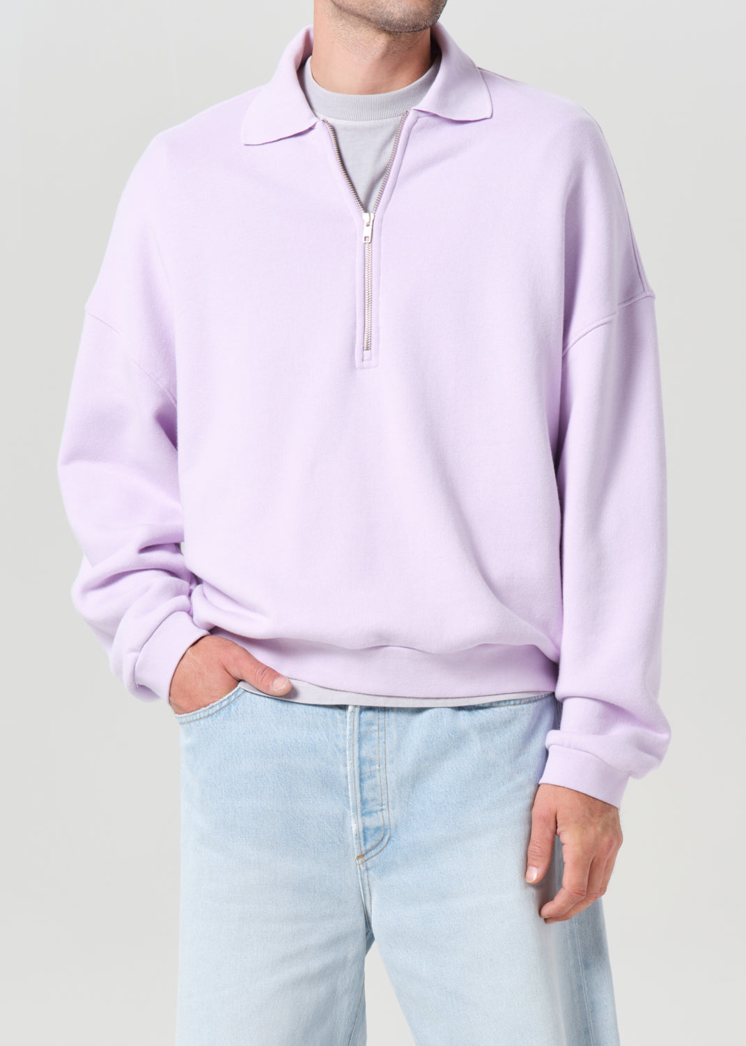 Person wearing a light purple half-zip sweatshirt and light blue jeans on a plain background