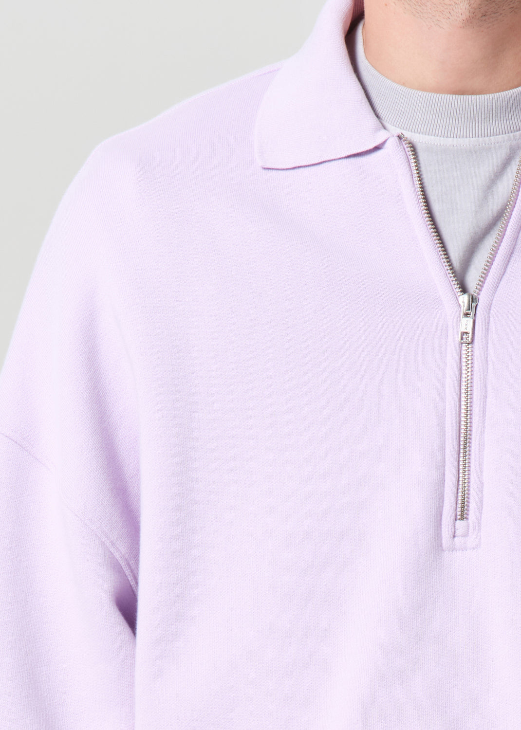 Close-up of a person wearing a light purple quarter-zip sweatshirt with a zipper.