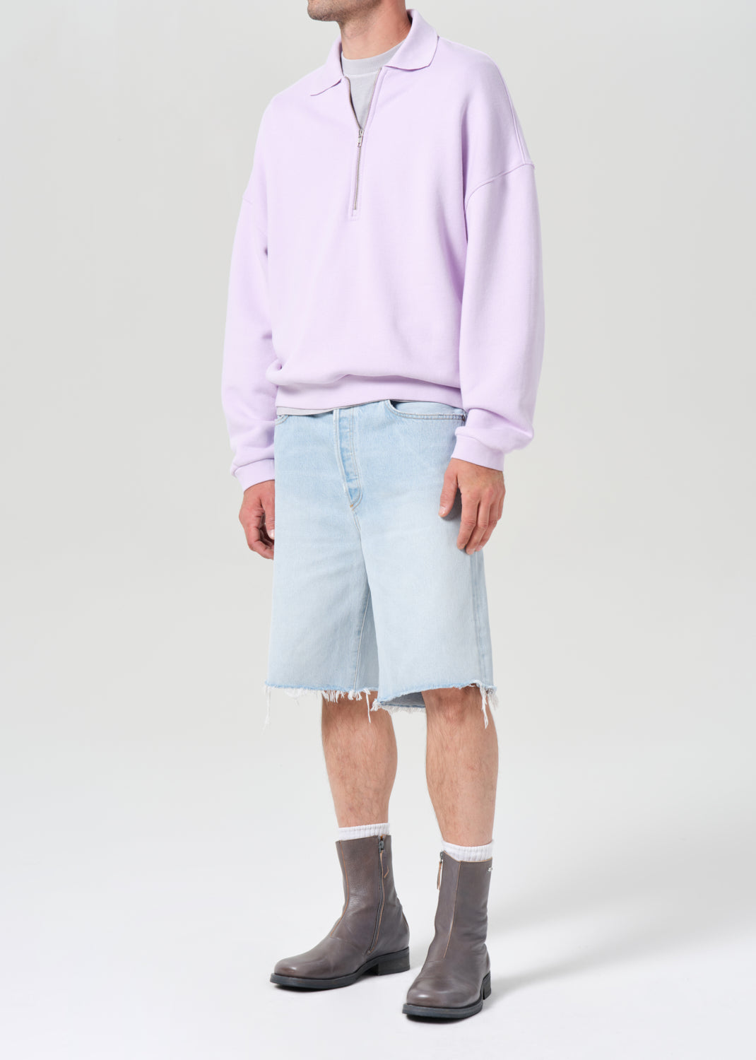 Person wearing a light purple shirt, light blue shorts, and gray shoes on a white background