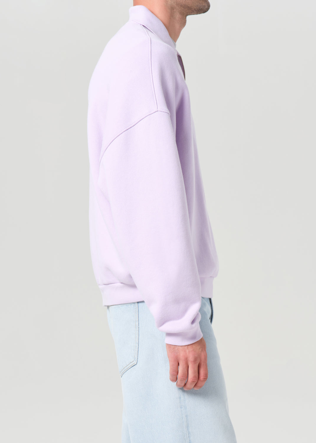 Person wearing a light purple sweater and light blue pants on a plain background