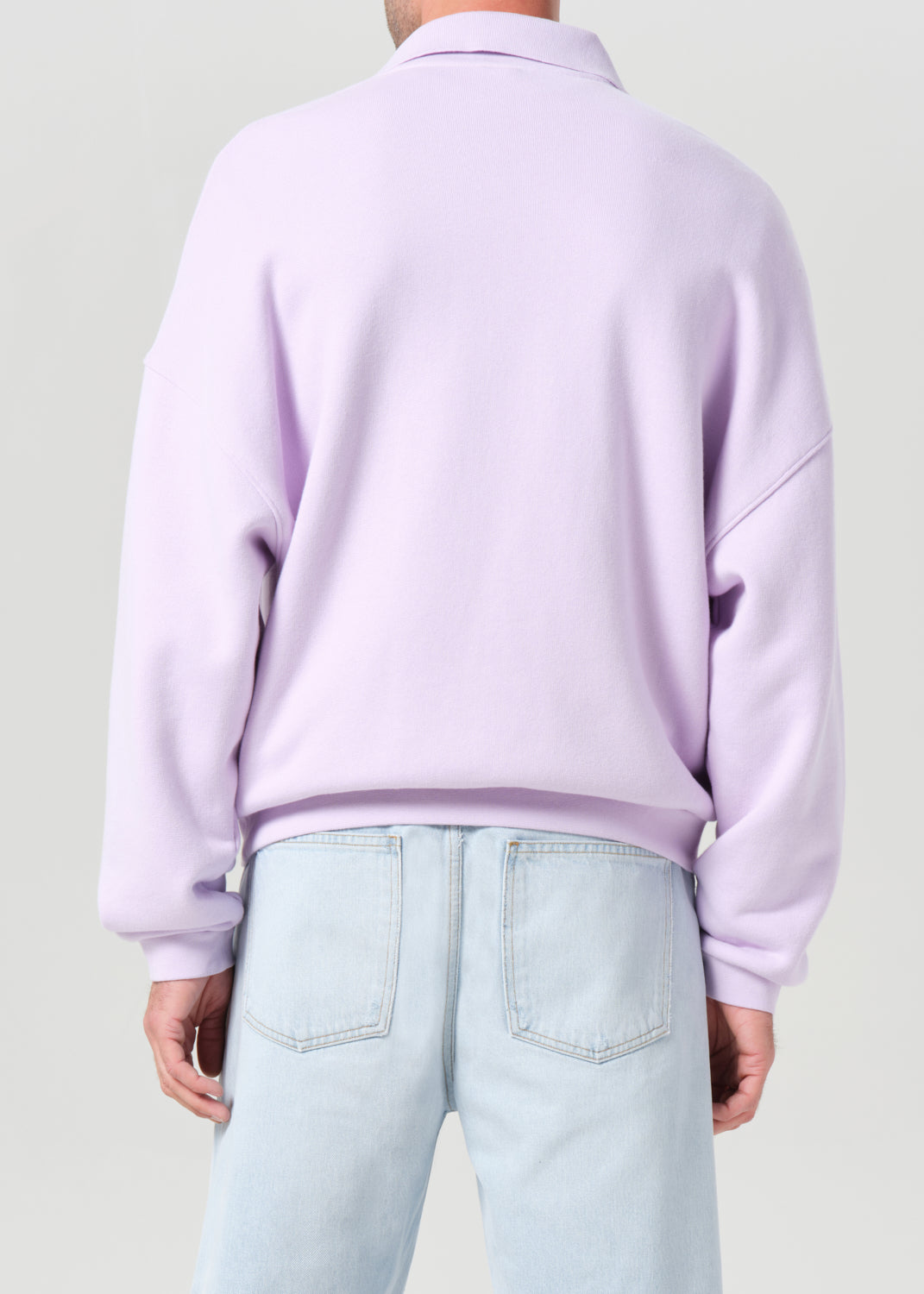 Person wearing a light purple sweater and light blue jeans on a plain background