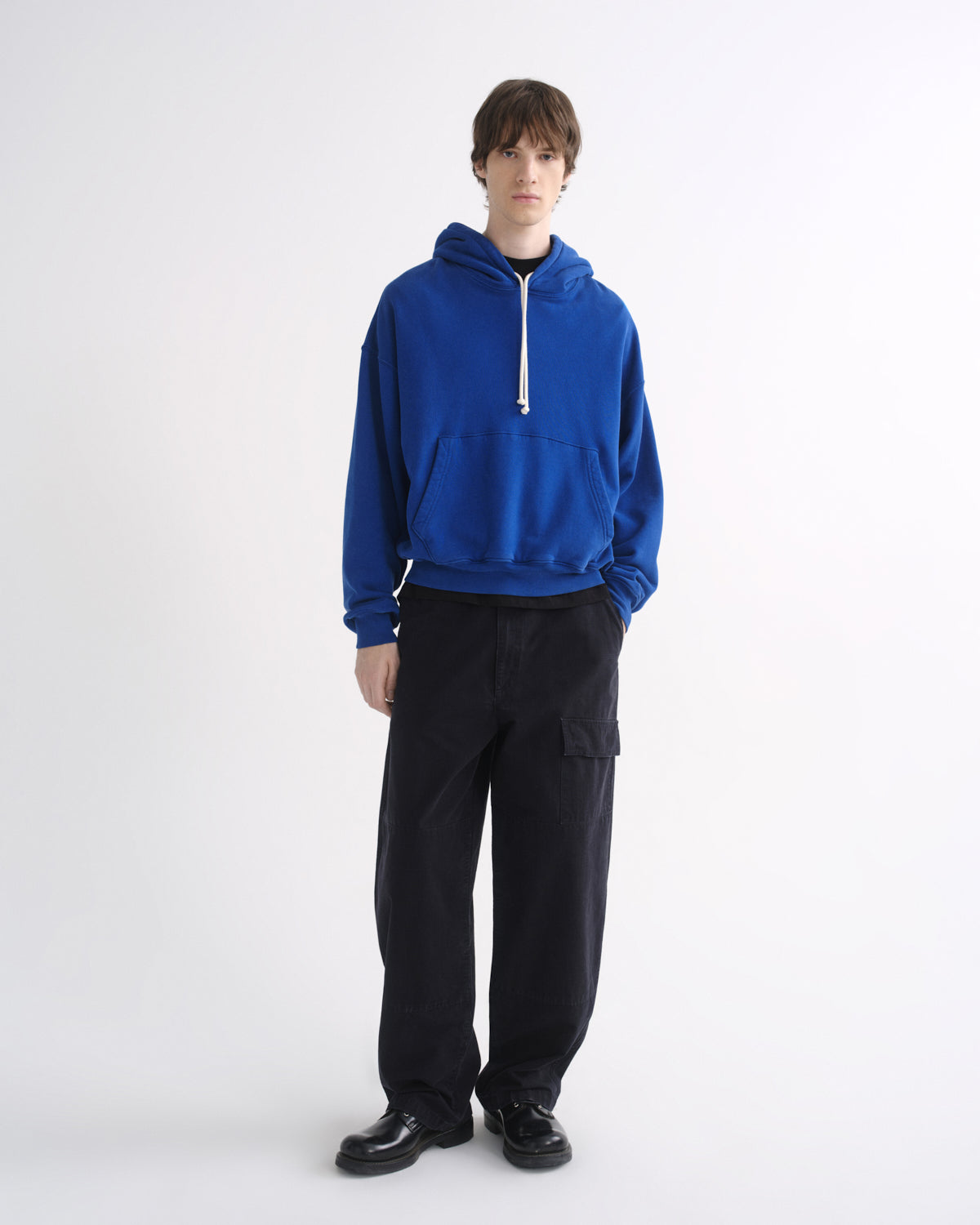 Person wearing a bright blue hoodie with black pants on a grey background