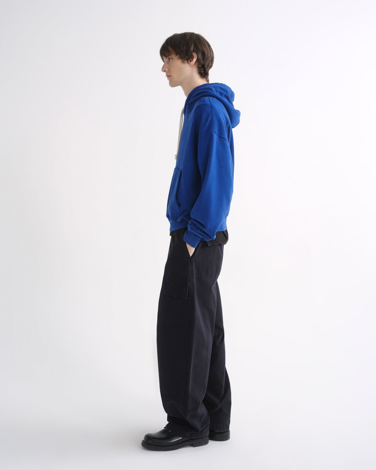 Person wearing a bright blue hoodie with black pants, side view, on a grey background