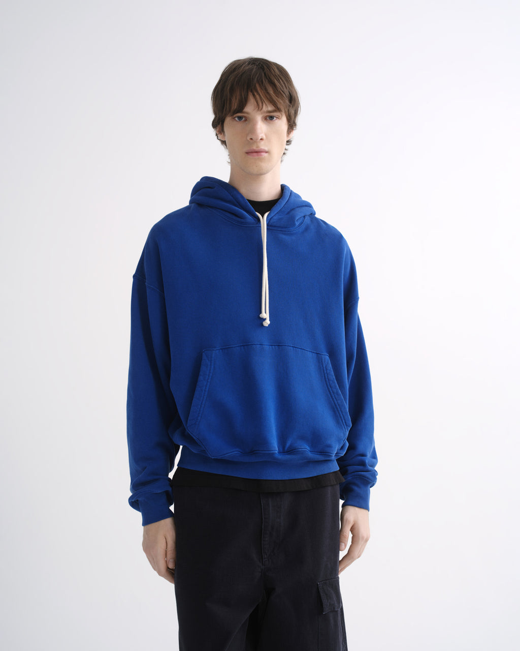 Person wearing a bright blue hoodie with black pants on a grey background