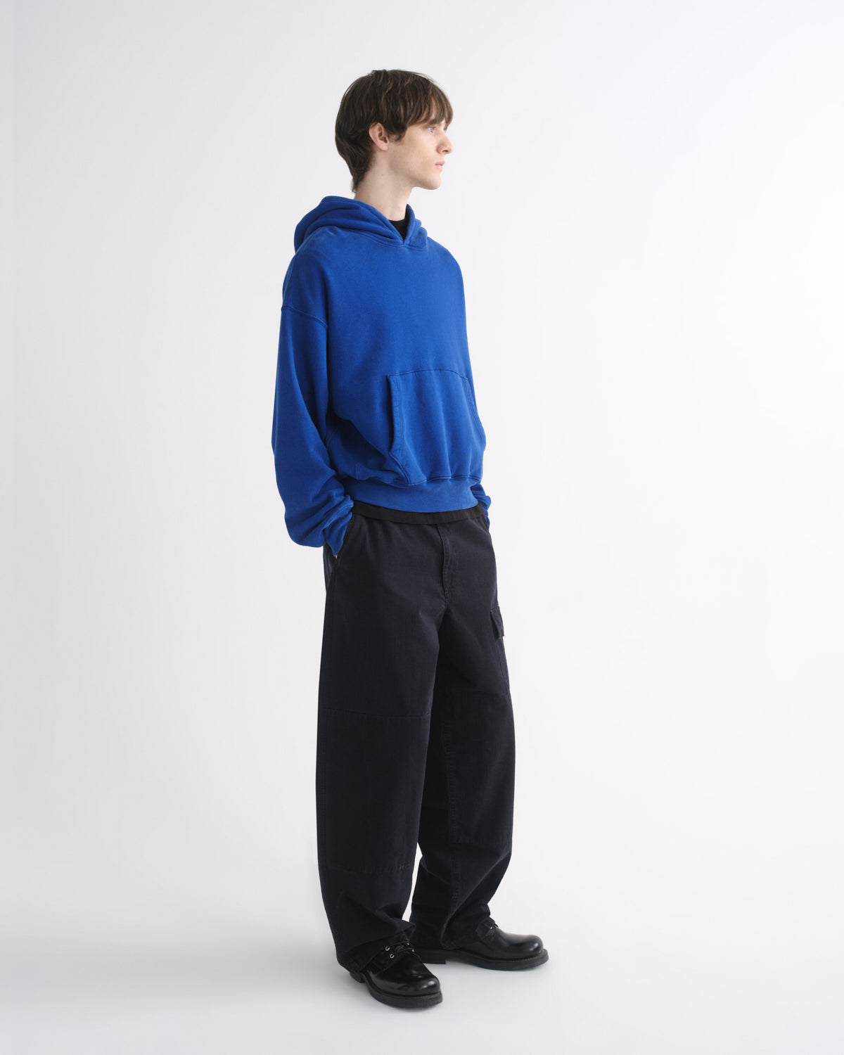 Person wearing a bright blue hoodie with black pants, side view, on a grey background