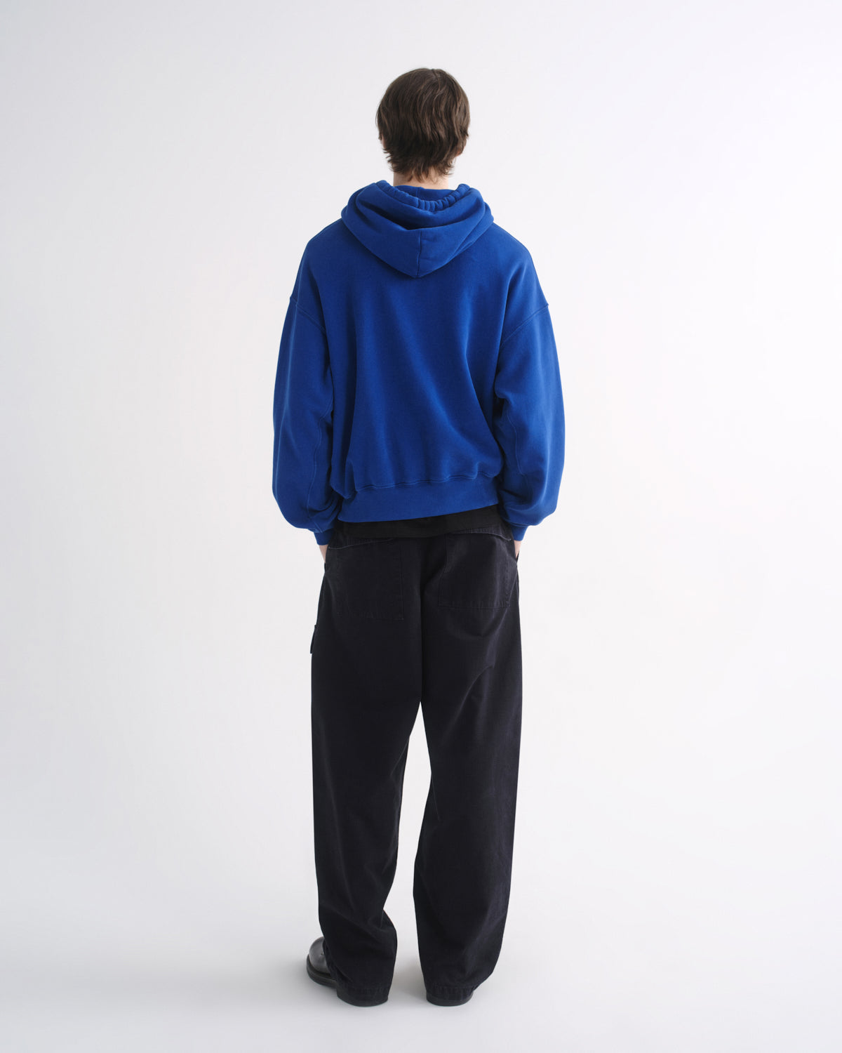 Person wearing a bright blue hoodie with black pants, back view, on a grey background