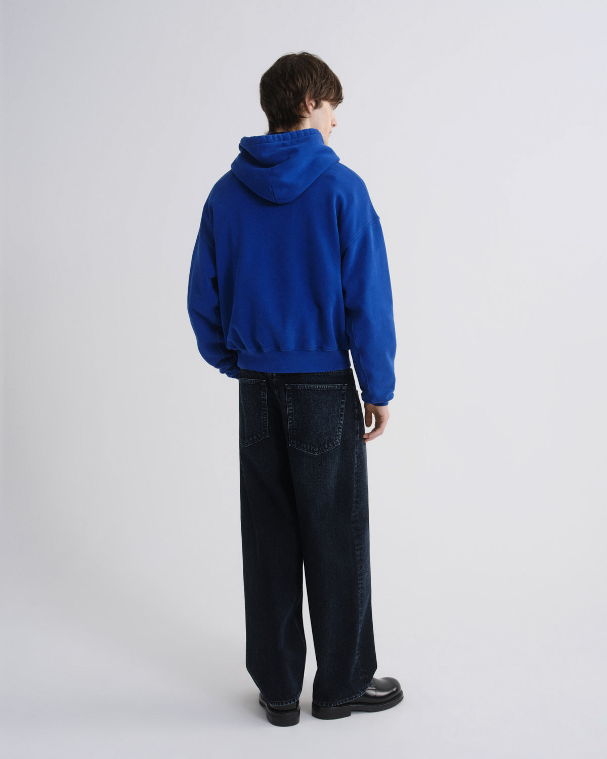 Person wearing a blue hoodie and black pants standing against a white background