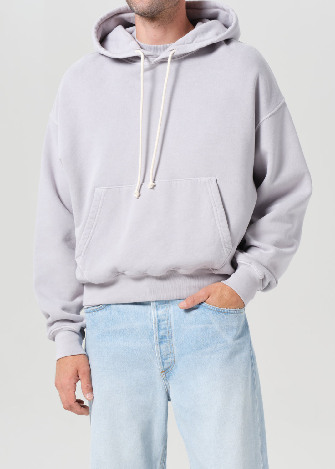 Person wearing a light gray hoodie and light blue jeans on a plain background