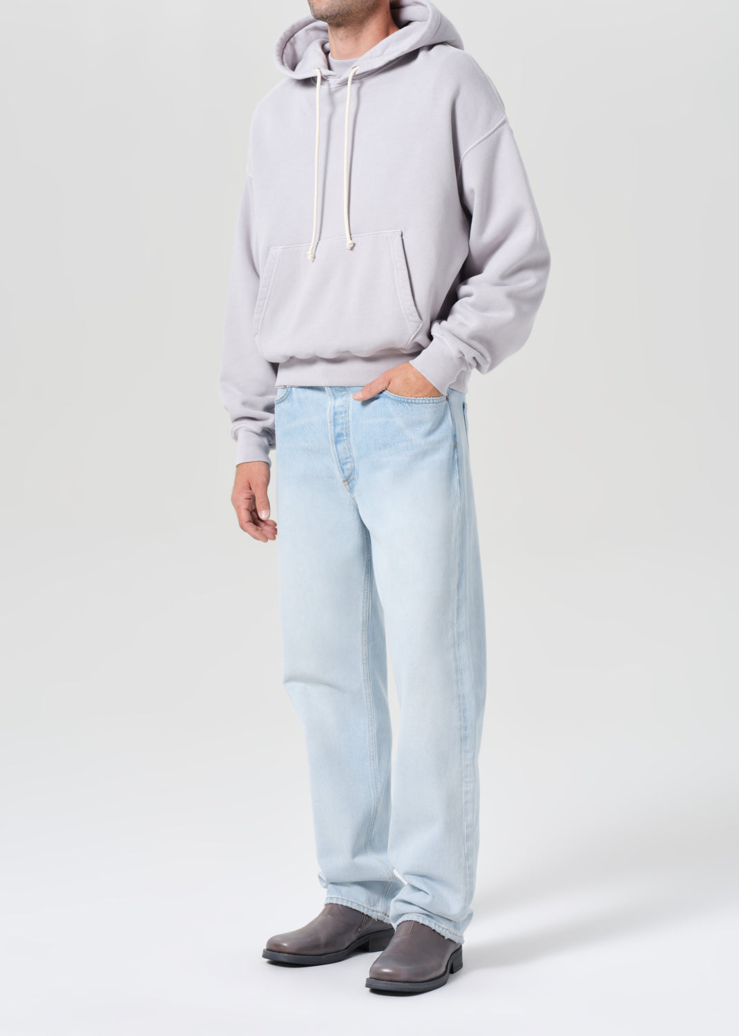 Person wearing a light gray hoodie and light blue jeans on a white background