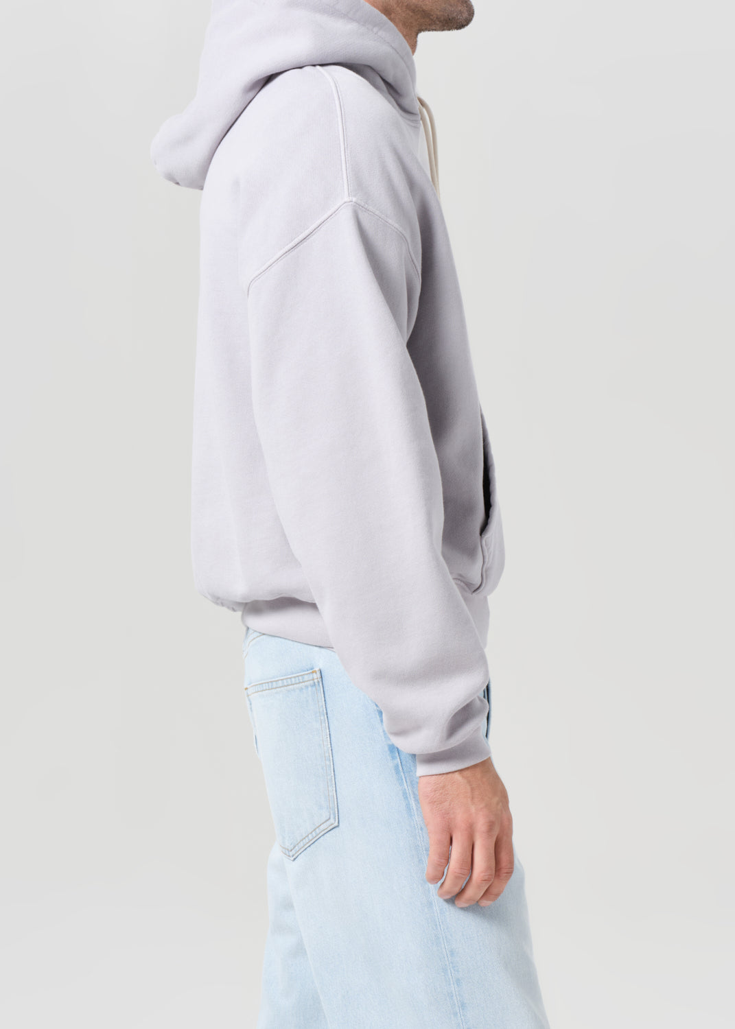 Person wearing a light gray hoodie and light blue jeans on a plain background