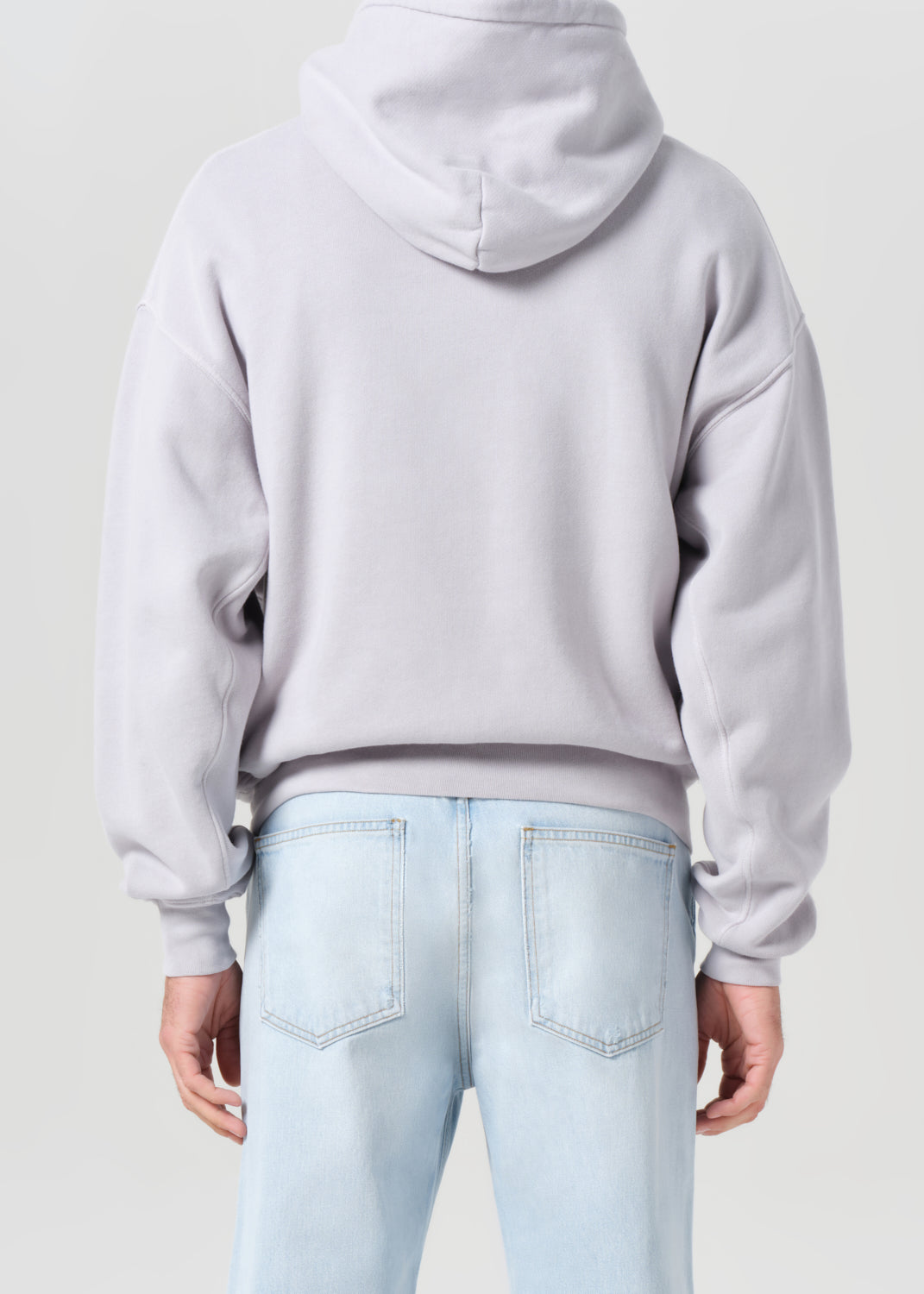 Person wearing a light gray hoodie and light blue jeans on a plain background