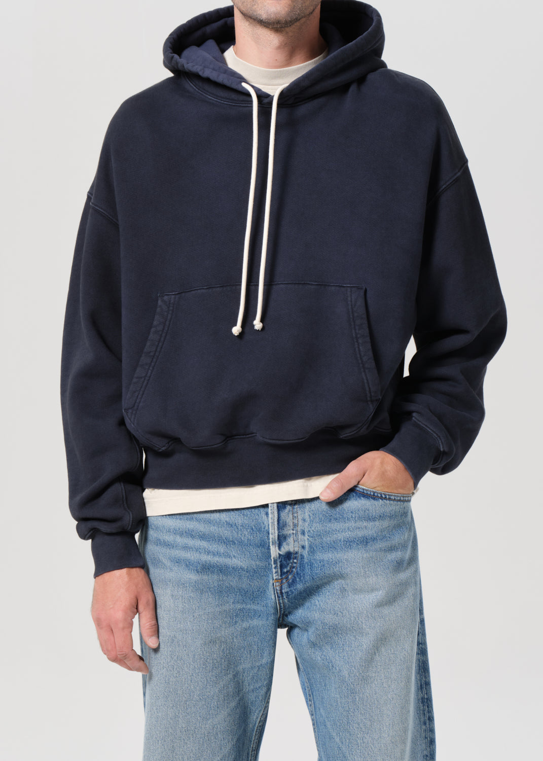 Person wearing a navy hoodie and blue jeans on a plain background