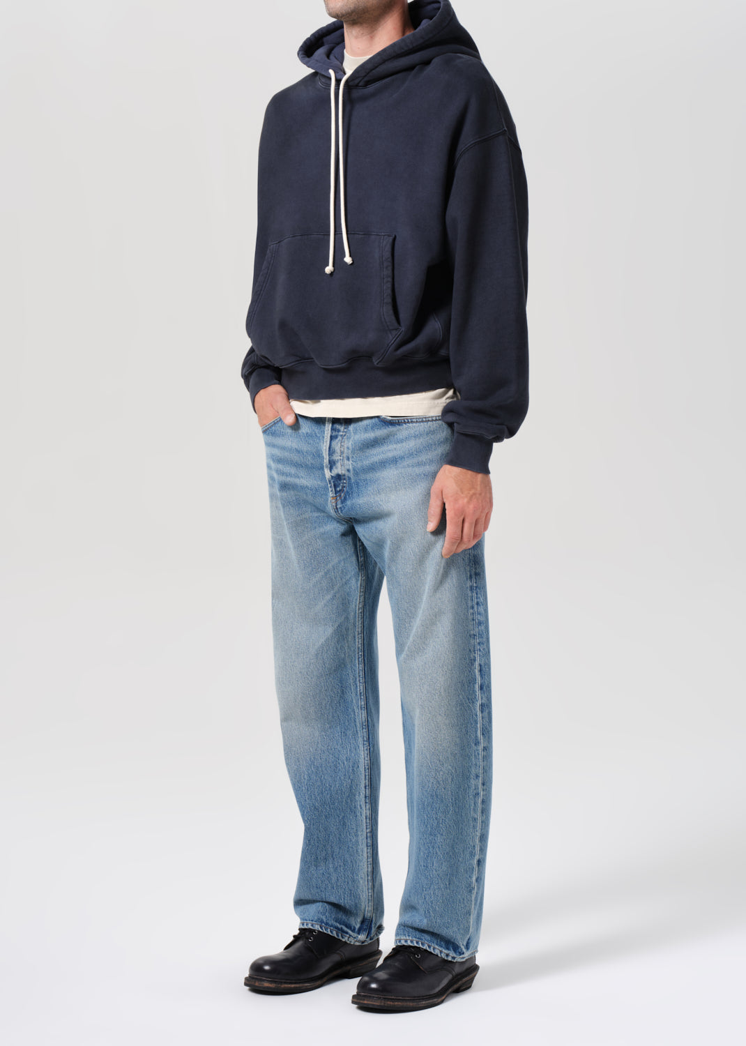 Person wearing a navy hoodie and light blue jeans on a white background