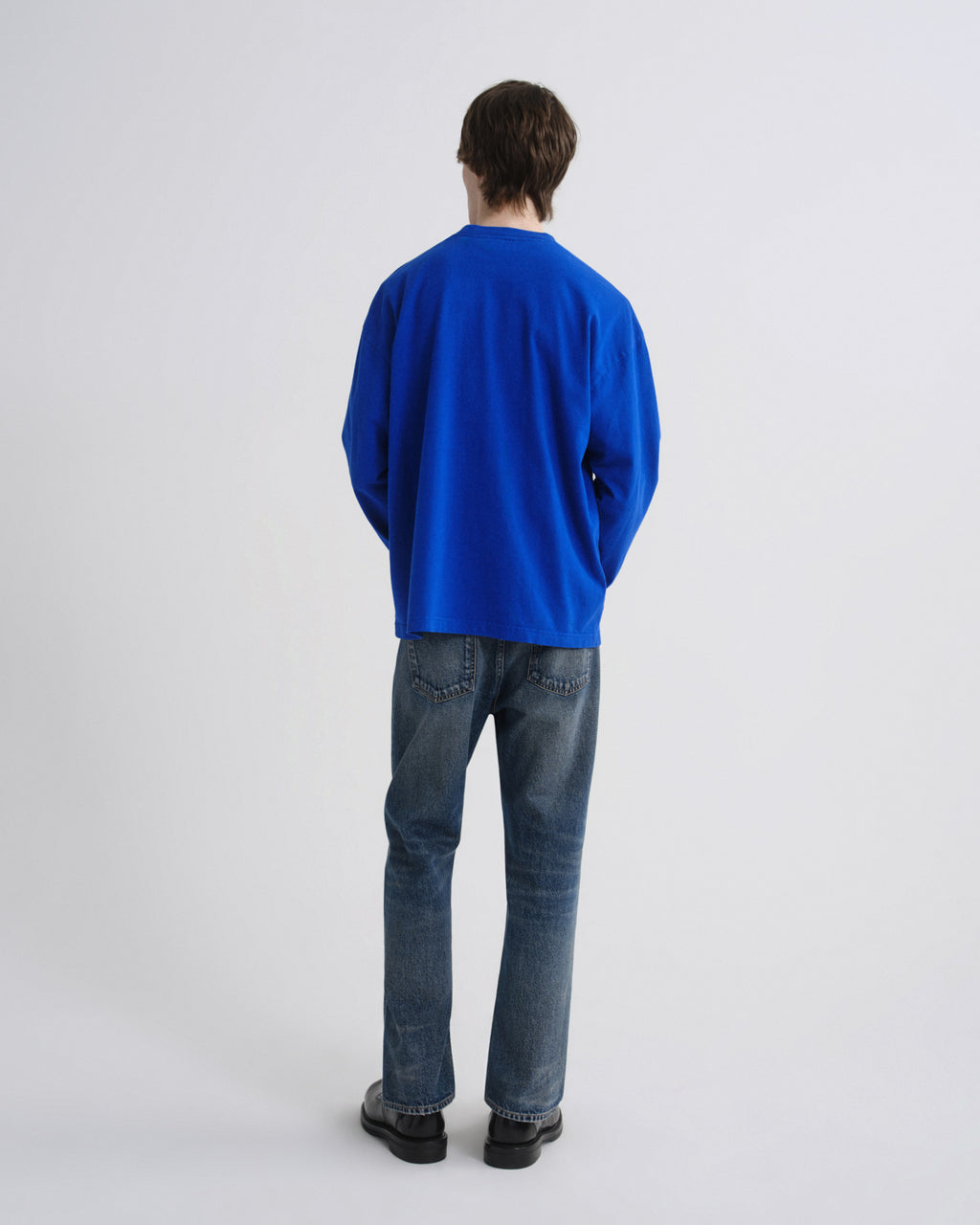 Person wearing a blue sweater and jeans on a grey background