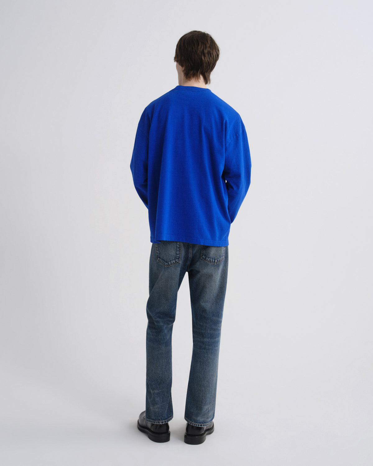 Person wearing a blue sweater and jeans on a grey background