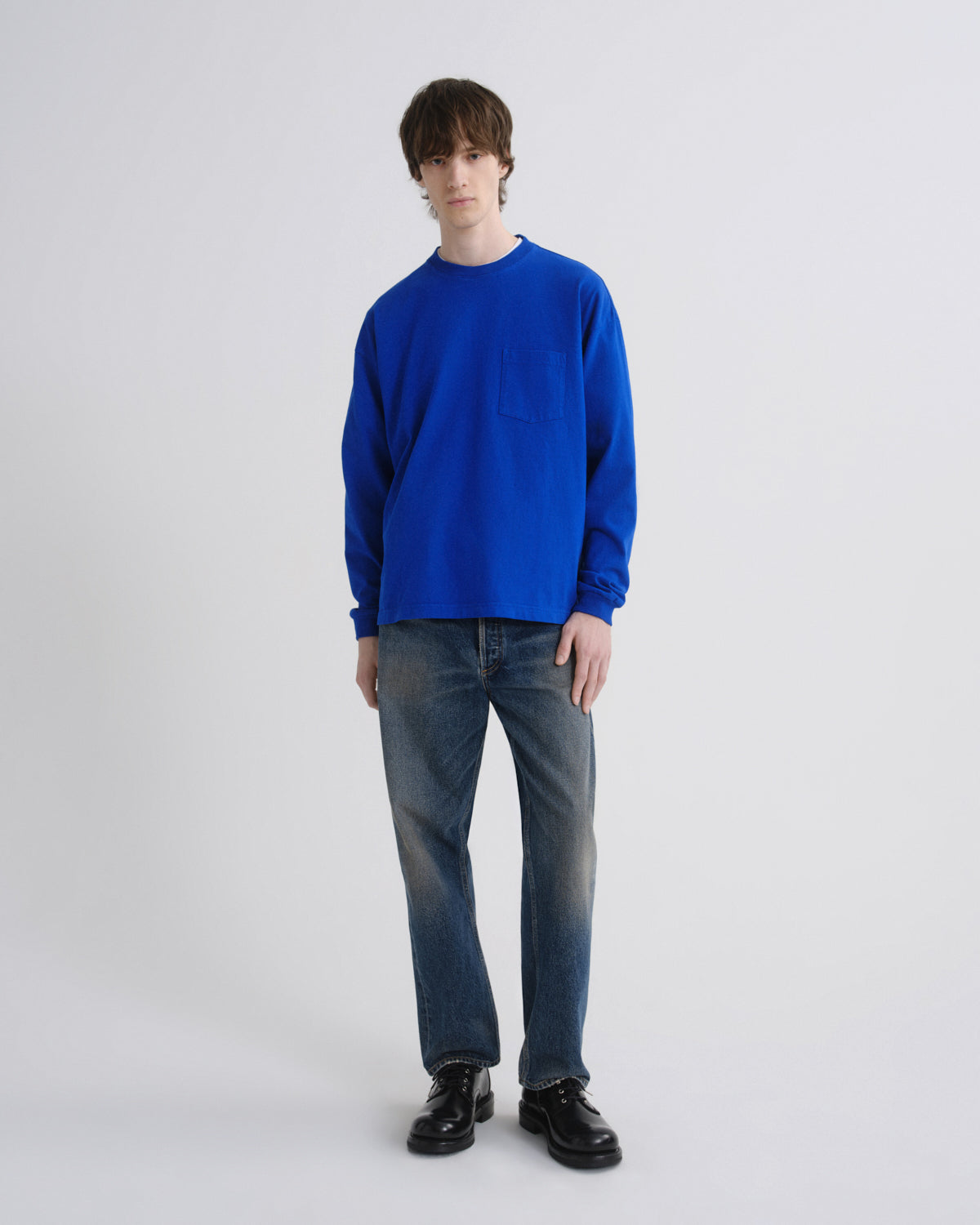 Person wearing a blue sweater and jeans on a grey background
