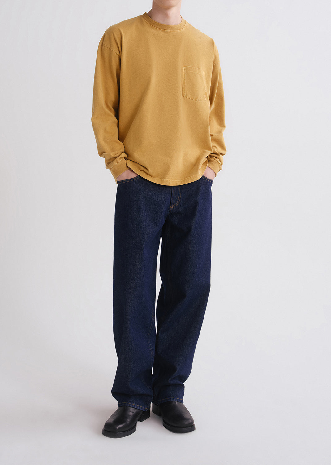 Person wearing a yellow shirt and blue jeans on grey background
