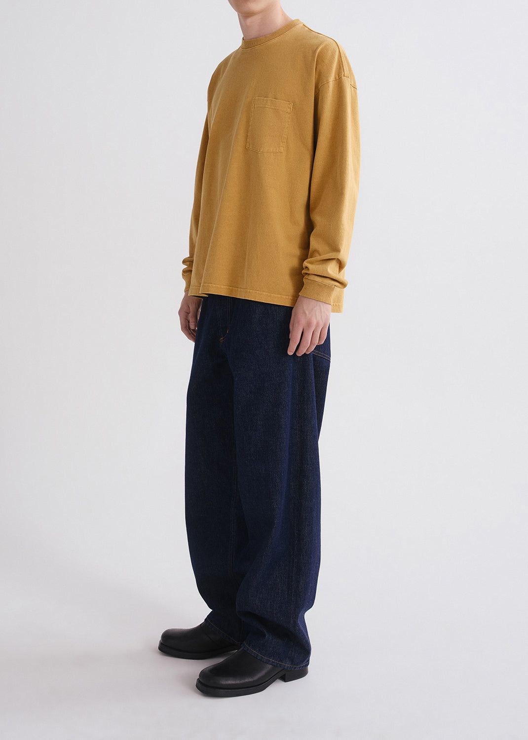 Person wearing a mustard yellow long-sleeve shirt and navy pants on a grey background
