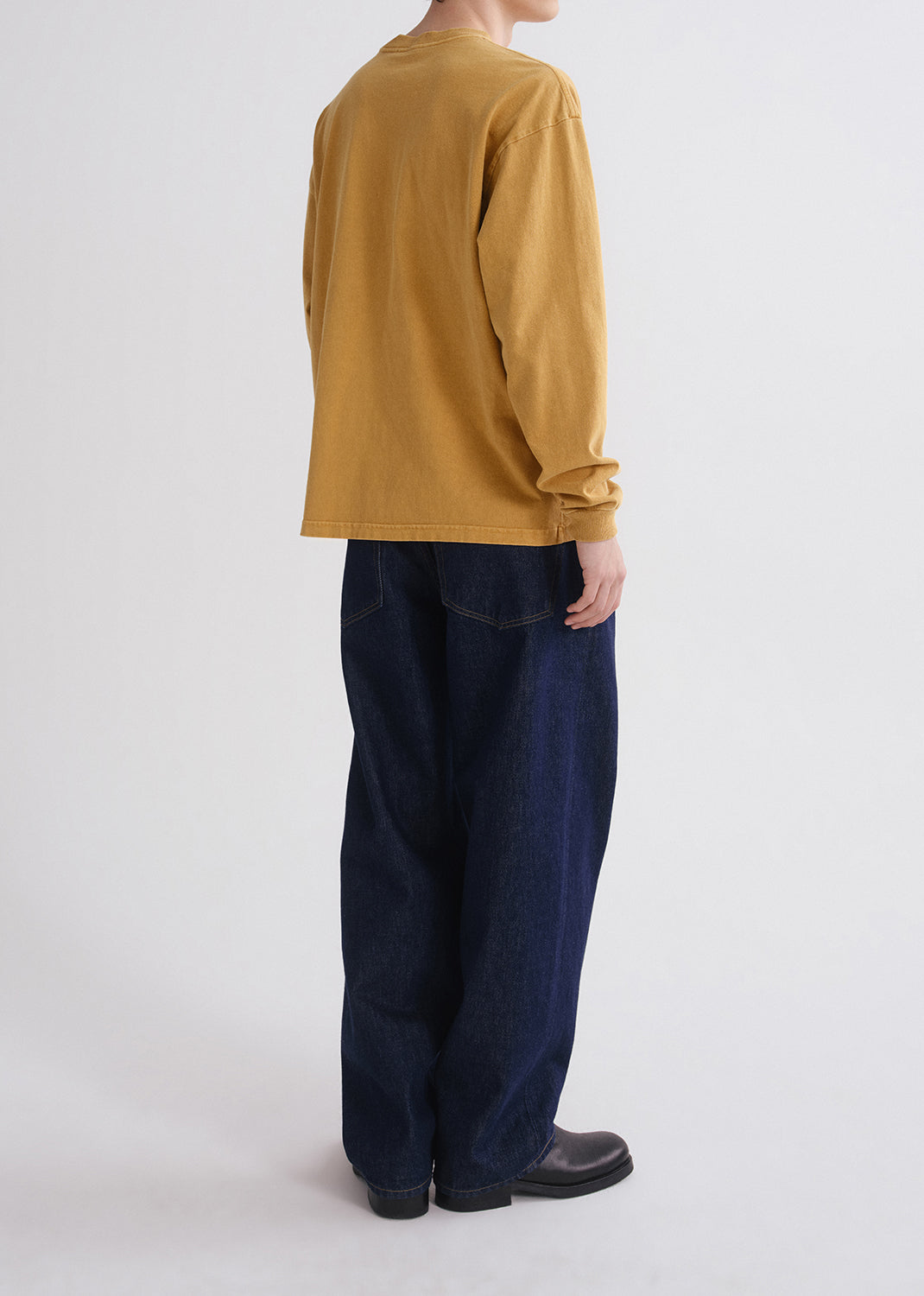 Person wearing a yellow shirt and blue jeans on grey background