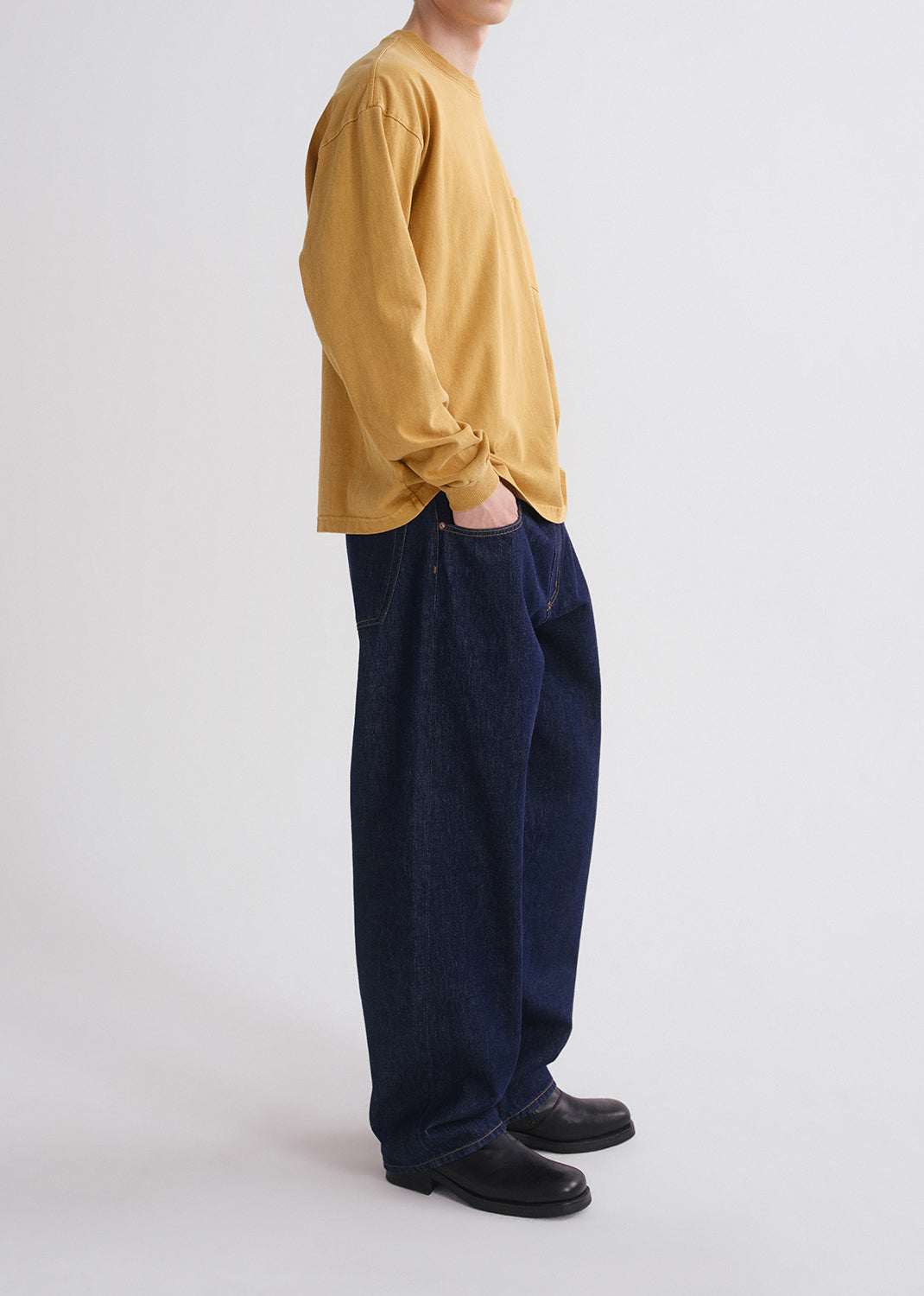Person wearing a yellow shirt and blue jeans on grey background