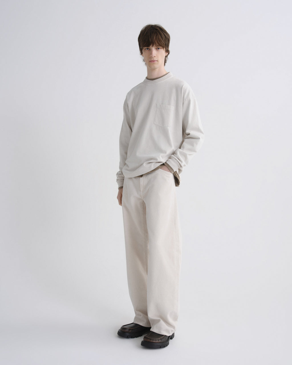 Person wearing a light gray sweater and beige pants on a white background