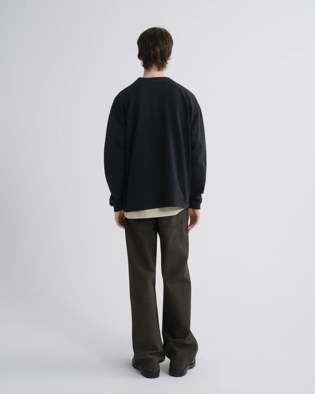 Person wearing a black sweater and dark pants on a white background