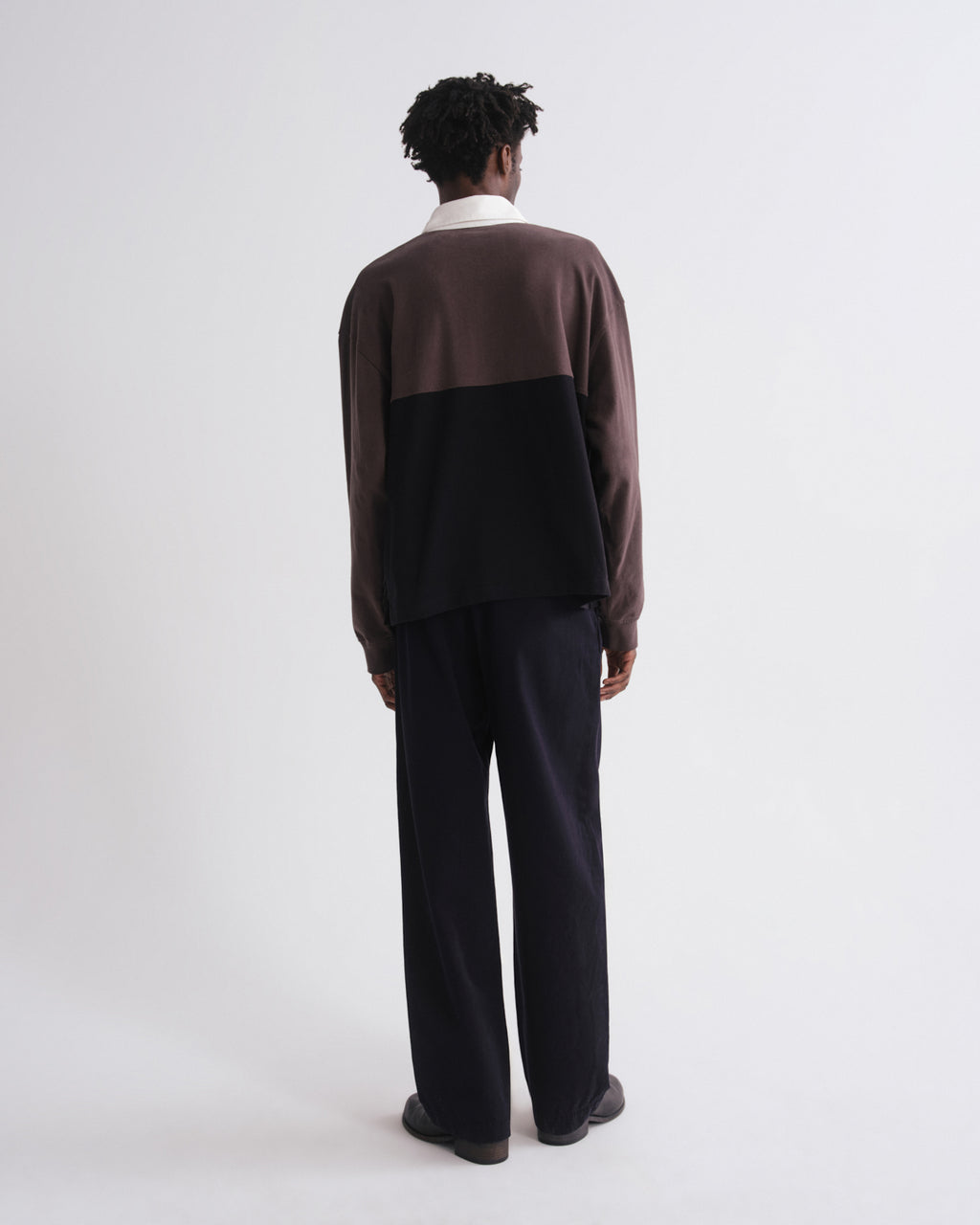 Person wearing a two-tone sweater and dark pants on a grey background