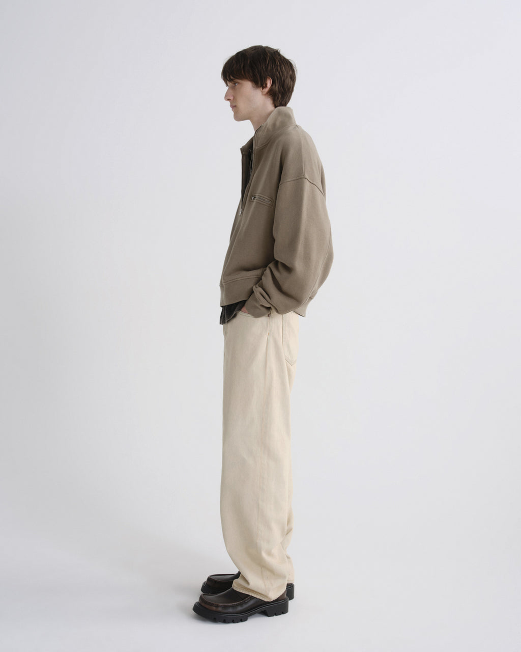 Person wearing a beige jacket and light-colored pants on a white background