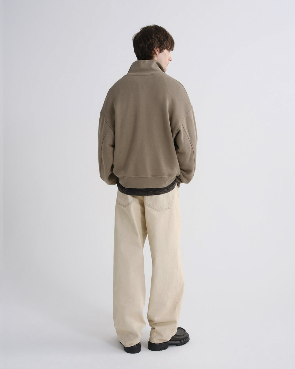 Person wearing a beige jacket and light-colored pants on a white background