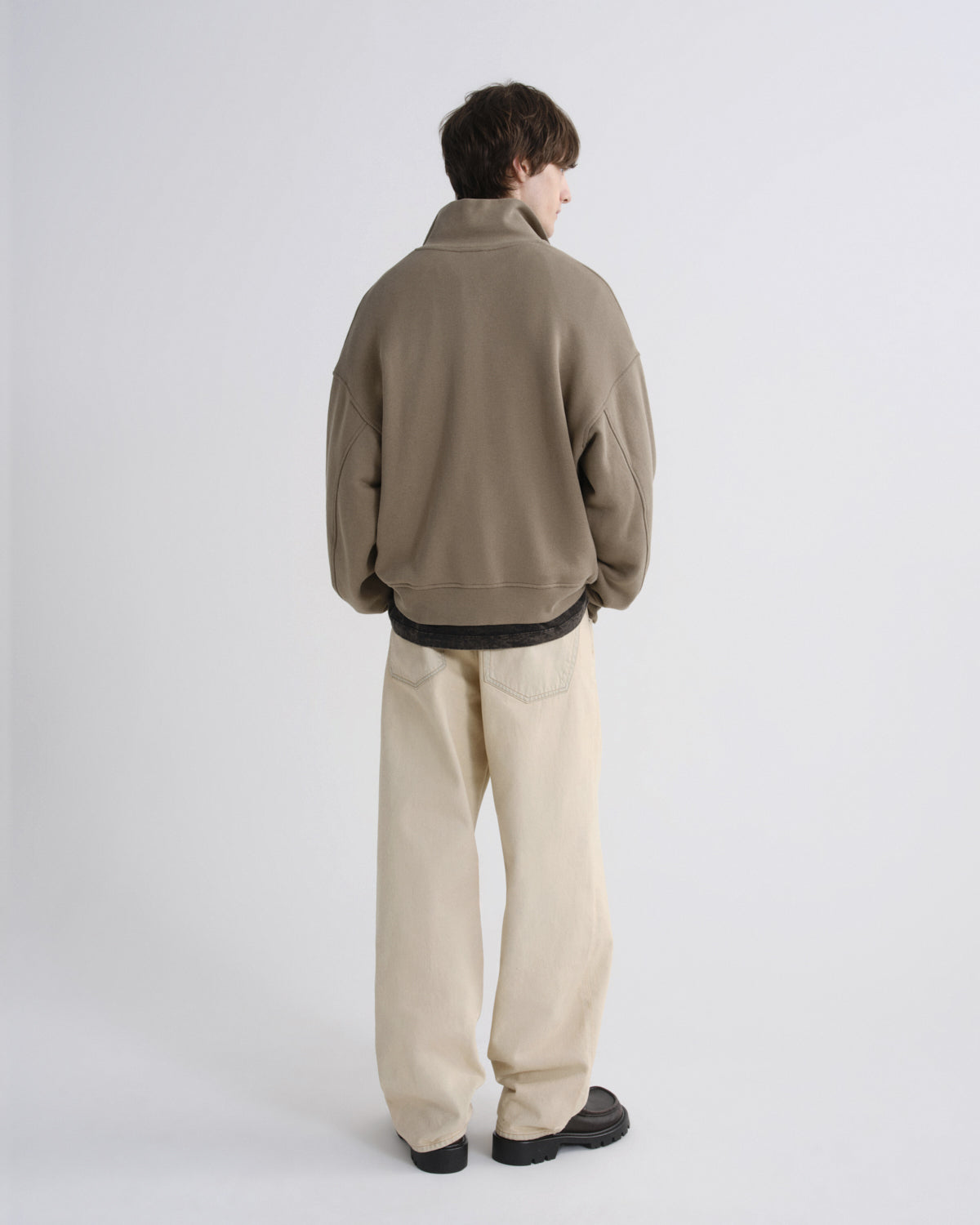 Person wearing a beige jacket and light-colored pants on a white background
