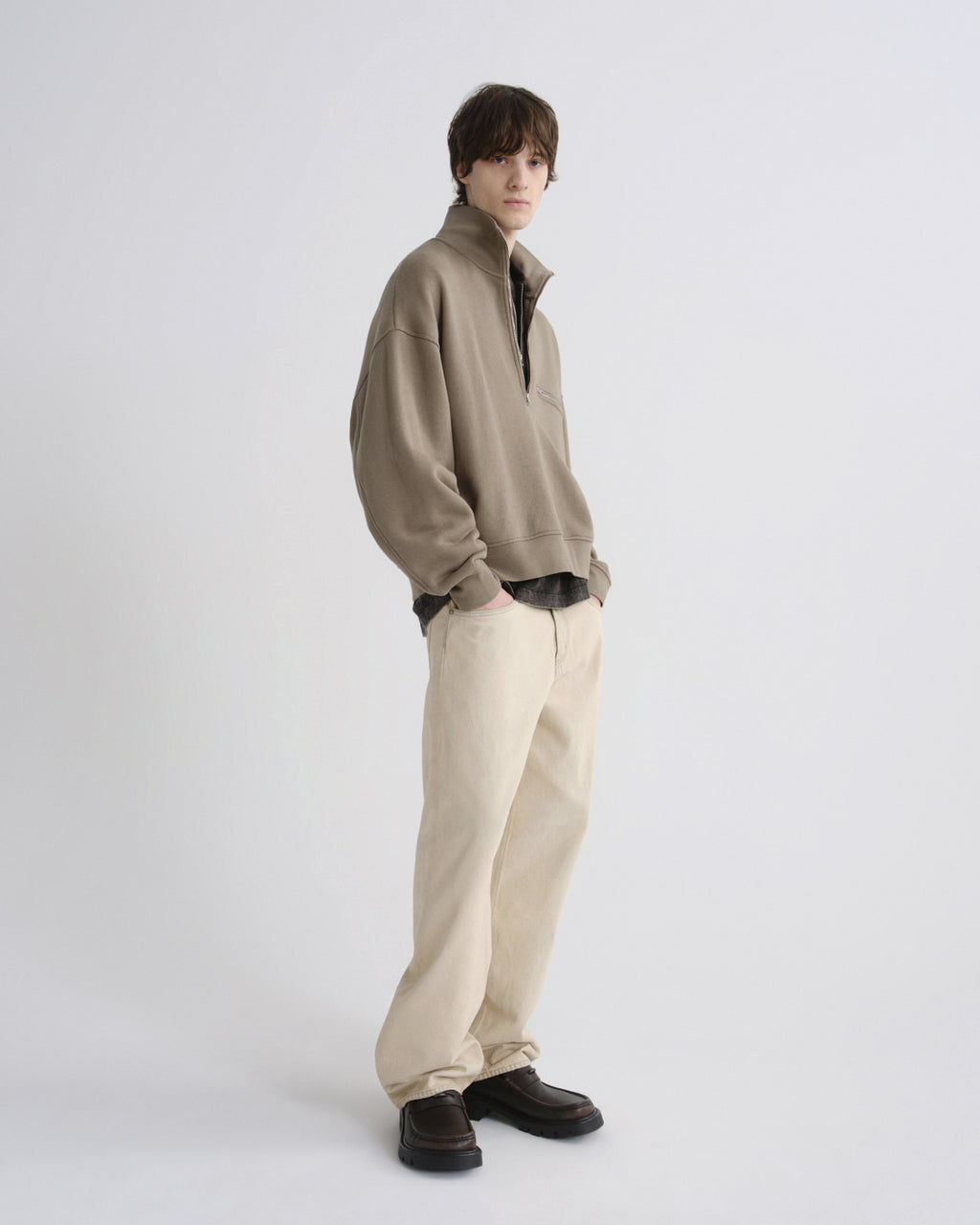 Person wearing a beige sweater and light-colored pants on a white background