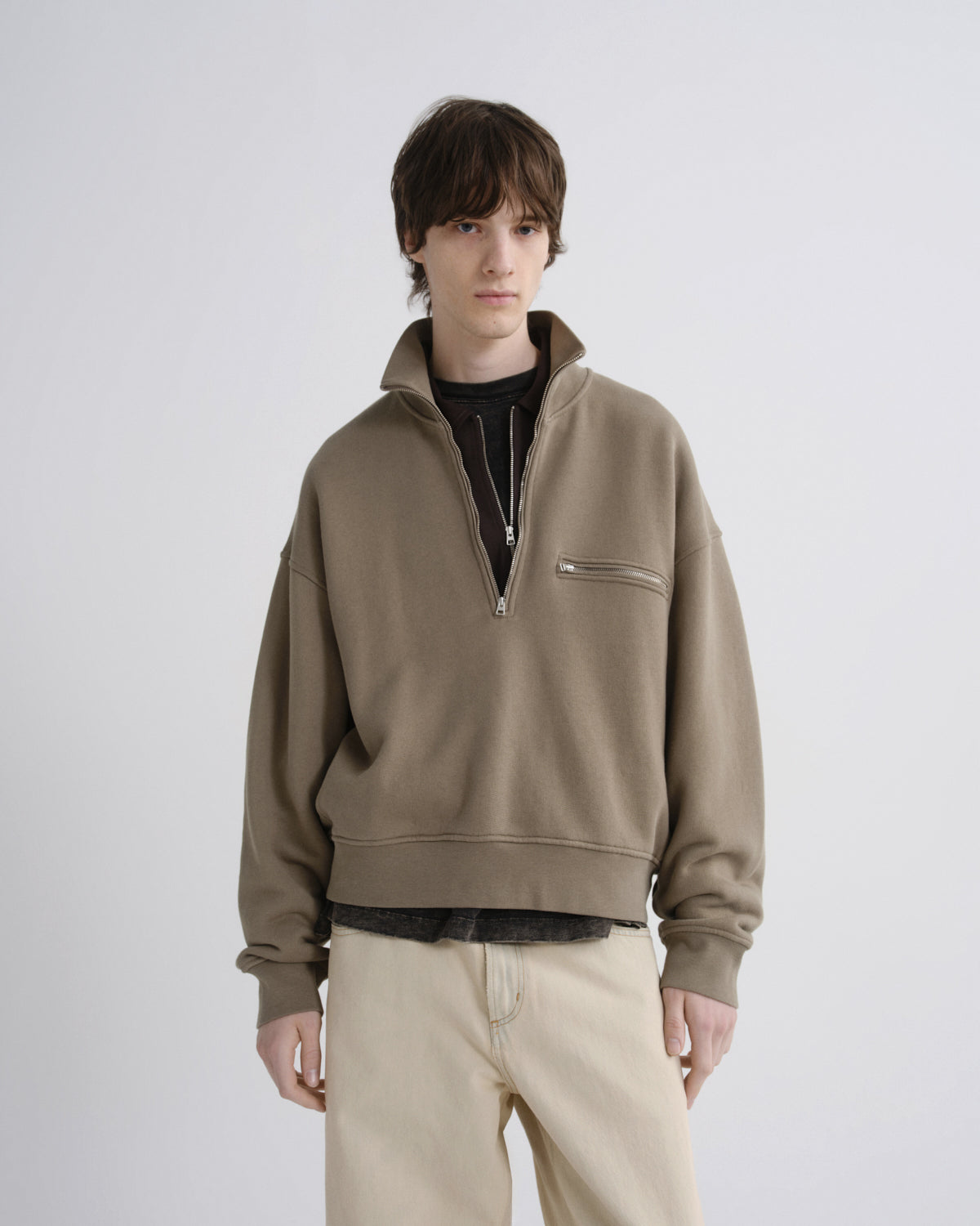 Person wearing a beige half-zip sweatshirt on a white background
