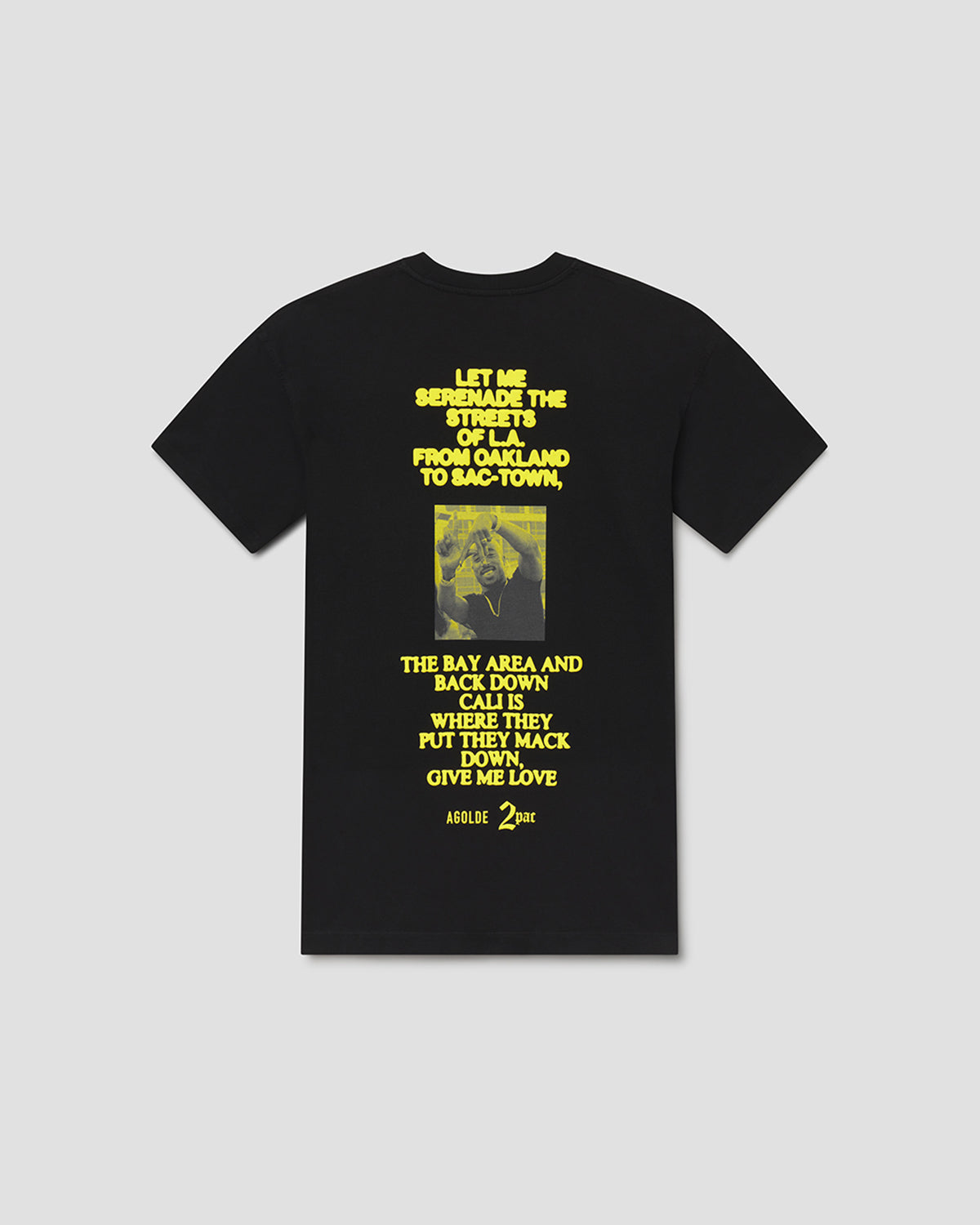 A black short-sleeve crewneck t-shirt with a yellow graphic print on the front, featuring a Bible verse and a small vintage-style photograph of a person, displayed against a neutral light gray background.