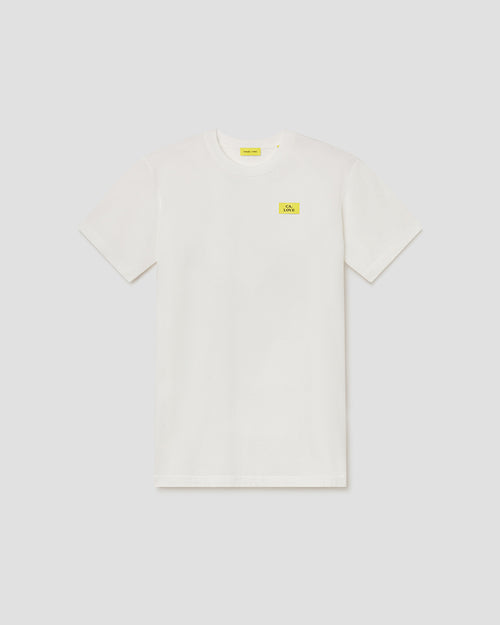 An off-white short-sleeve crewneck t-shirt with a small yellow rectangular logo patch on the left chest, displayed flat against a light gray background.