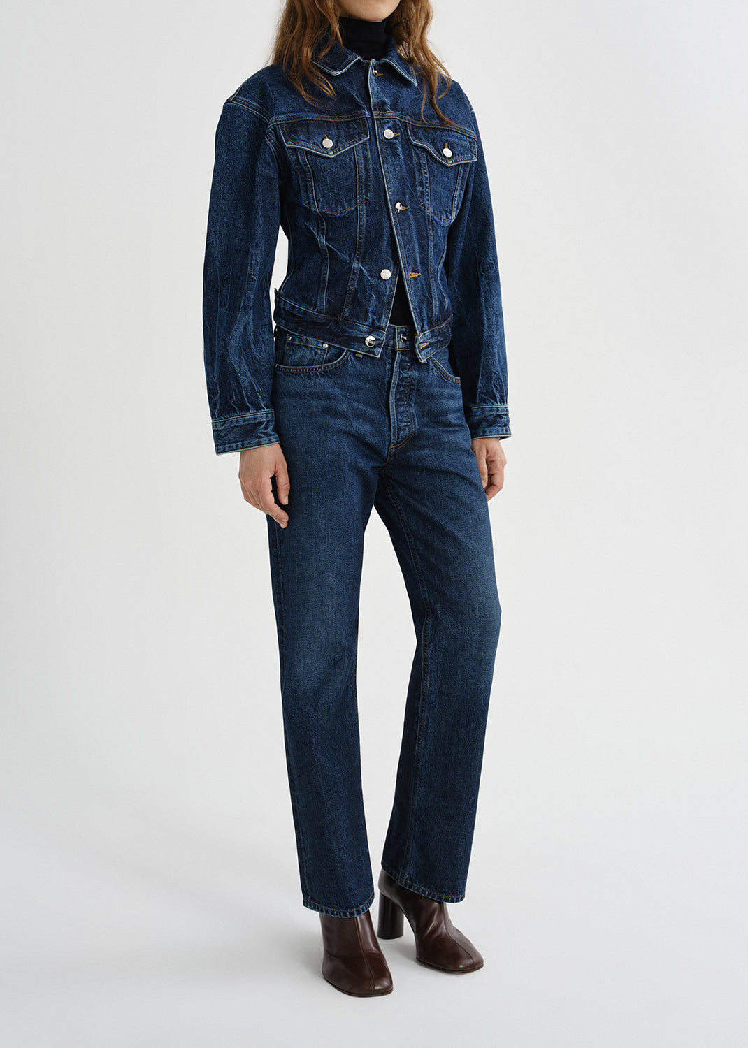 Person wearing a dark wash denim jacket with matching dark wash straight leg jeans on a grey background