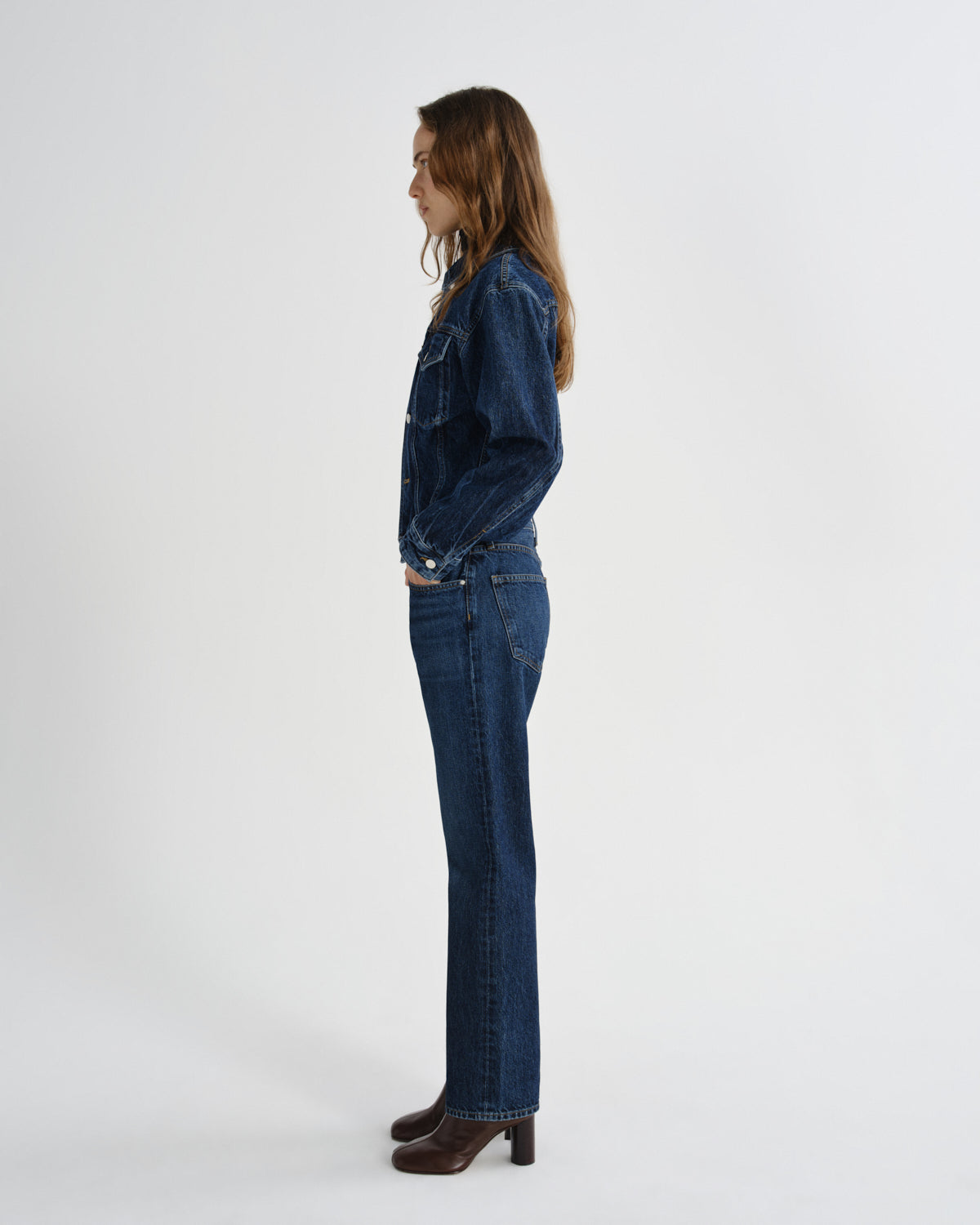 Person wearing a dark blue denim jacket and jeans on a white background