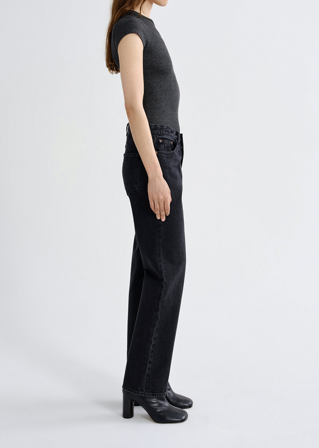 Person wearing a dark gray t-shirt and black jeans on a grey background