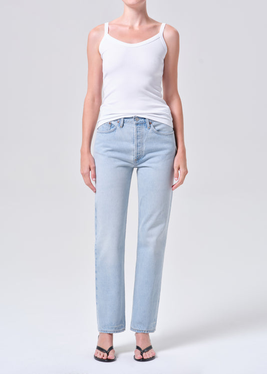 Person wearing light blue jeans and a white tank top on a plain background