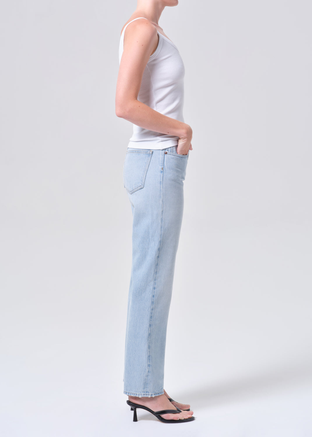 Person wearing light blue jeans and a white top on a plain background