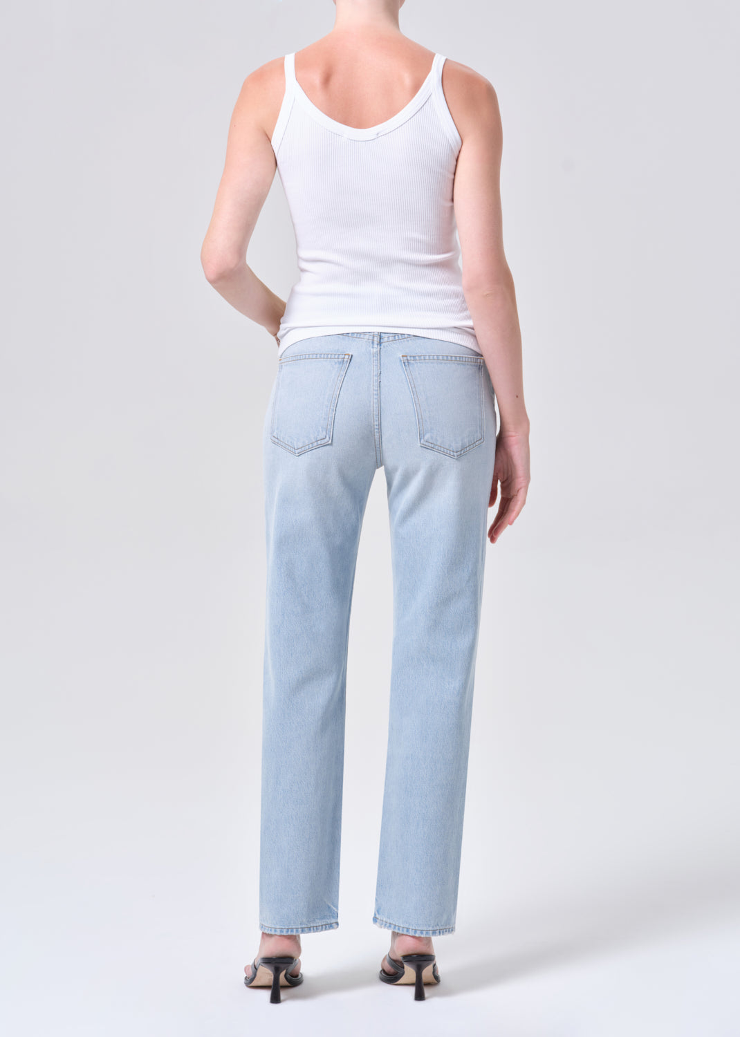 Person wearing light blue jeans and a white tank top on a plain background