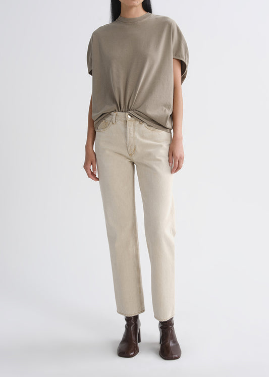 Person wearing a beige top and pants with brown shoes on a grey background