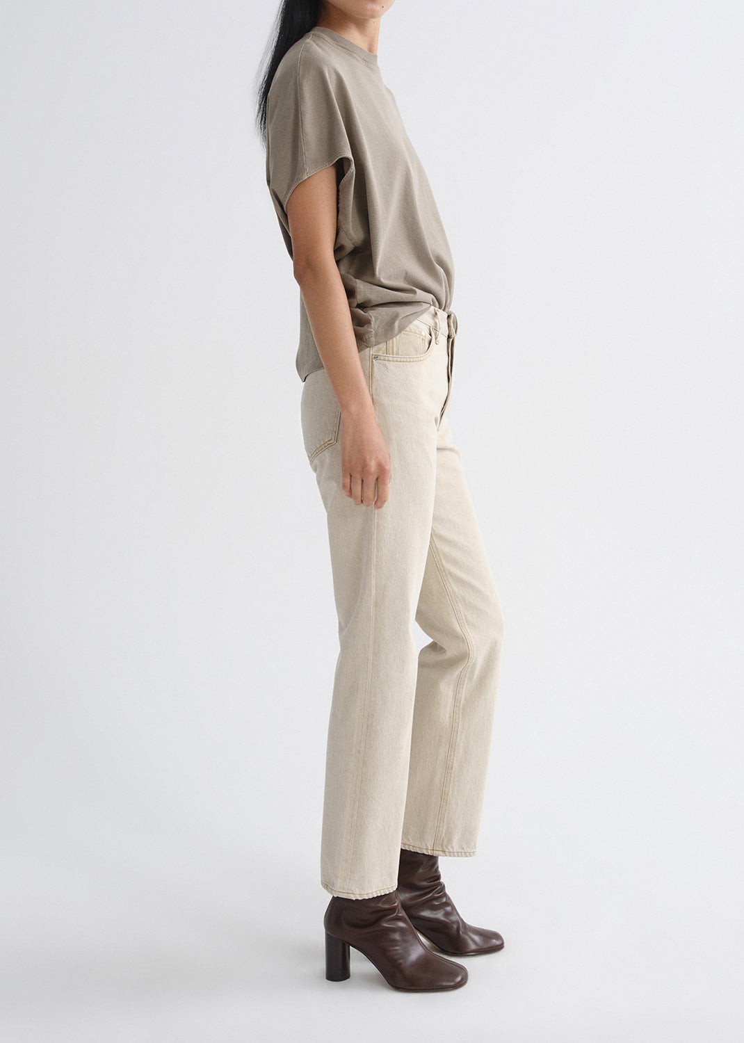 Person wearing a beige t-shirt, light-colored pants, and brown shoes on a grey background