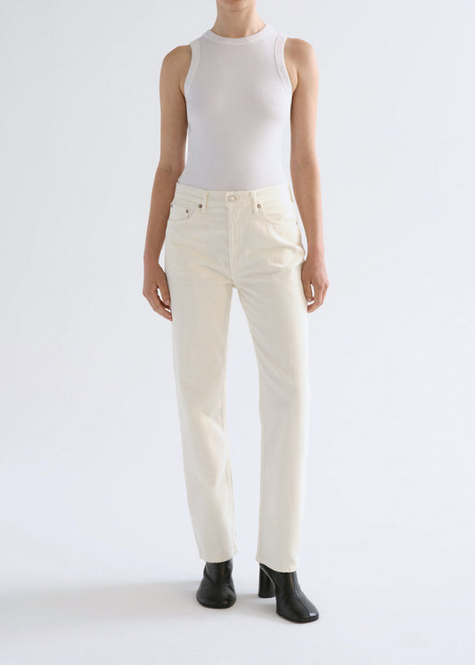 Person wearing a white sleeveless top and cream-colored pants on a grey background