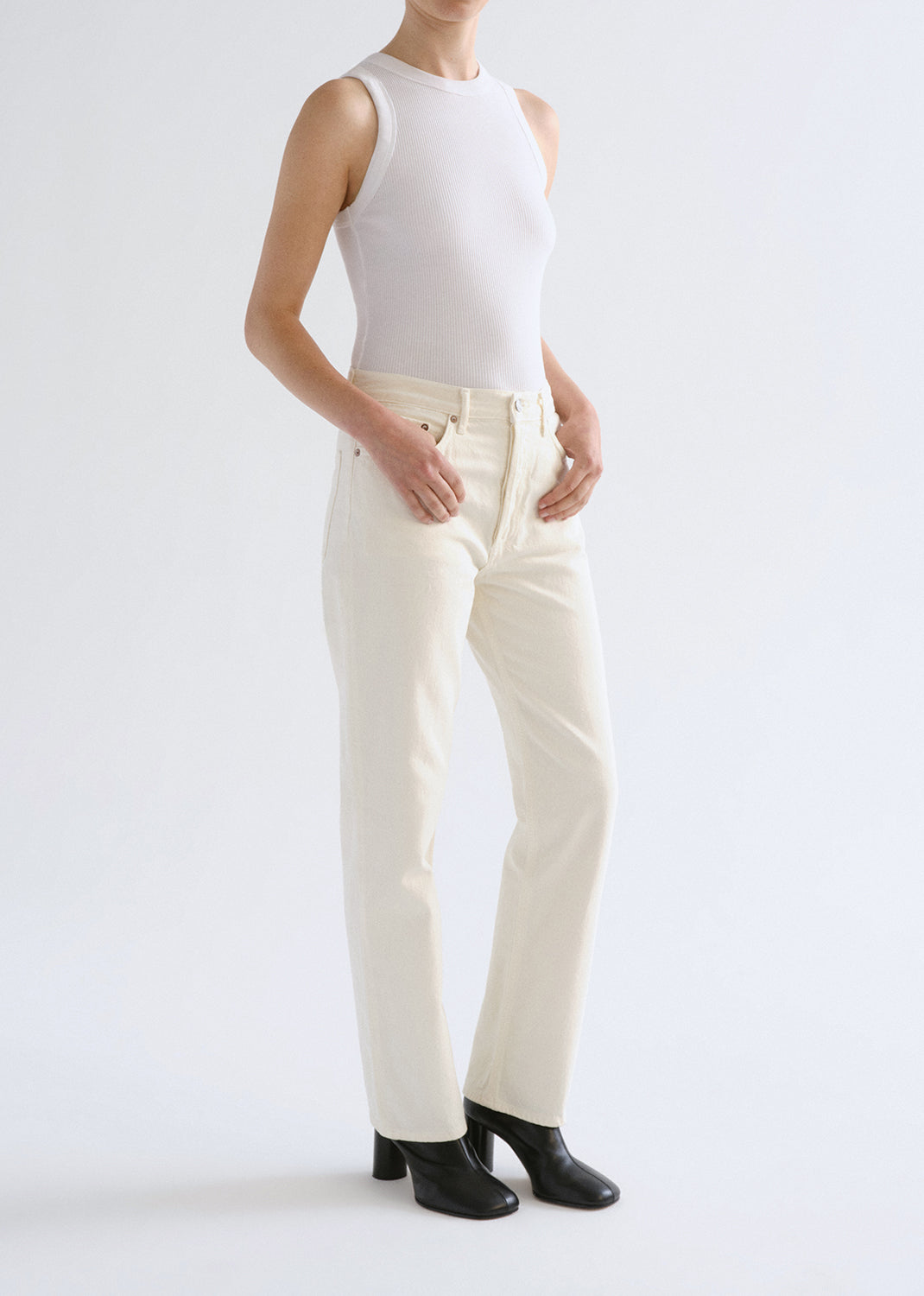 Person wearing a white sleeveless top and cream pants on a light grey background