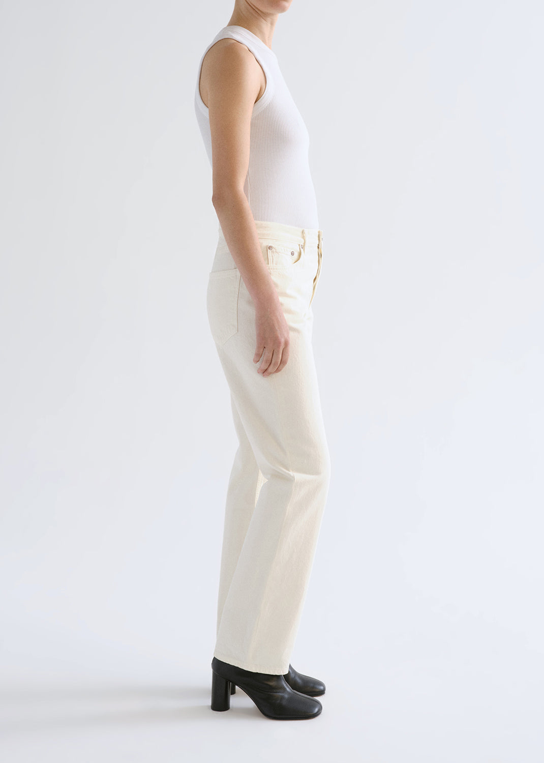 Person wearing a white sleeveless top and cream pants on a grey background