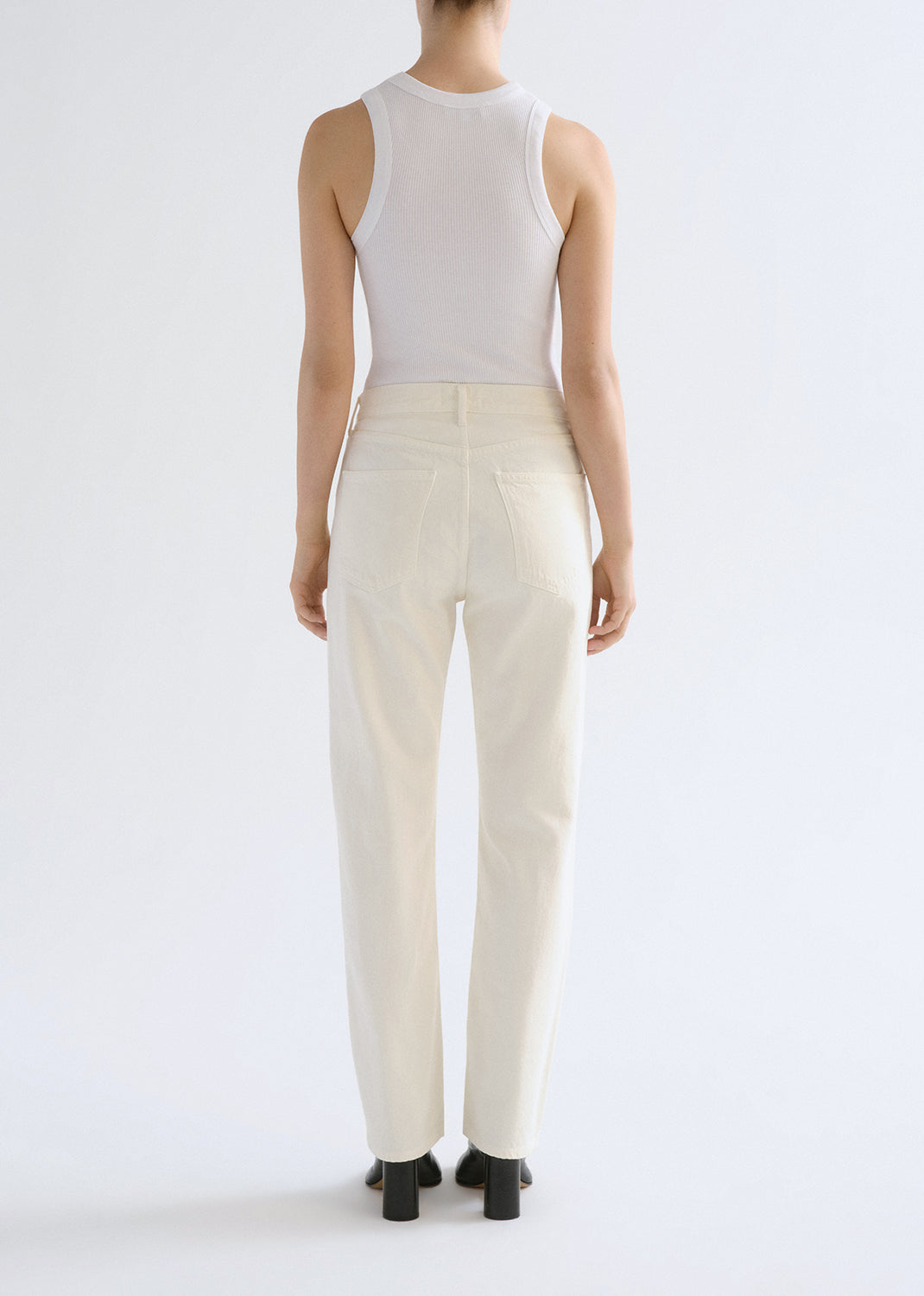 Person wearing a white sleeveless top and cream-colored pants on a grey background