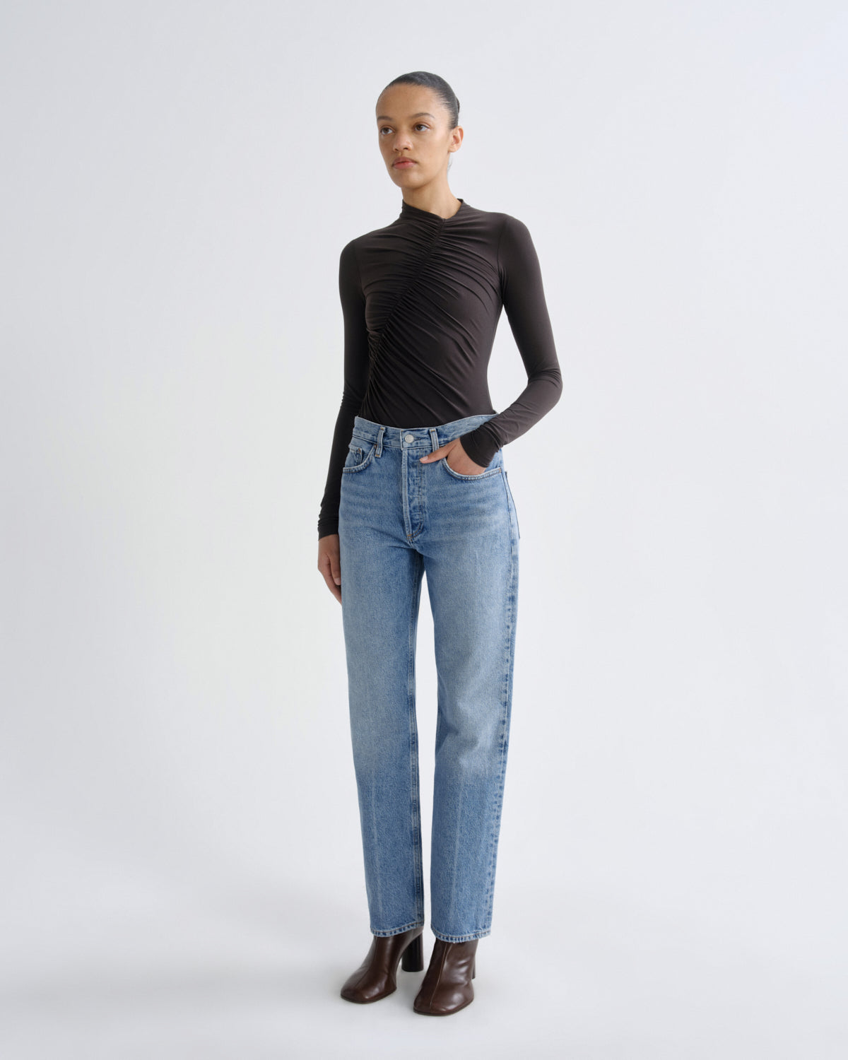 Person wearing a black long-sleeve top and blue jeans on a white background